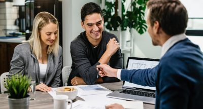 Young happy couple going through housing plans with real estate agent. Happy couple having a meeting with real estate agent and analyzing blueprints while communicating.