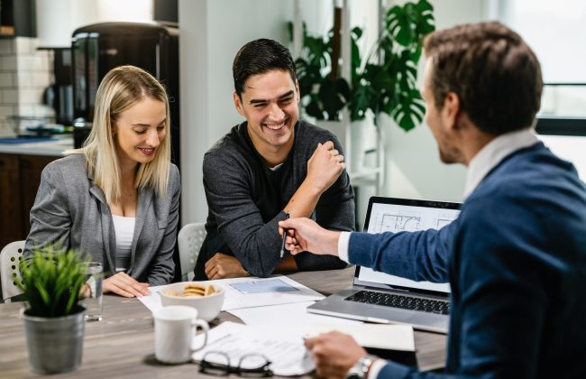 Happy couple having a meeting with real estate agent and analyzing blueprints while communicating.