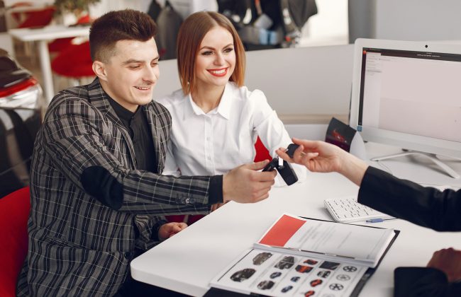 People in a car salon. Couple buying the car. Elegant women with handsome man. Manager helps people.